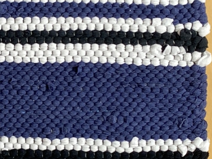 Detail image of blue, white, and black stripes of a rag rug. Shows how some rags hide the warp and others cover it.